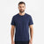A man wearing a plain navy blue short-sleeve crewneck t-shirt, standing against a clean white studio background.