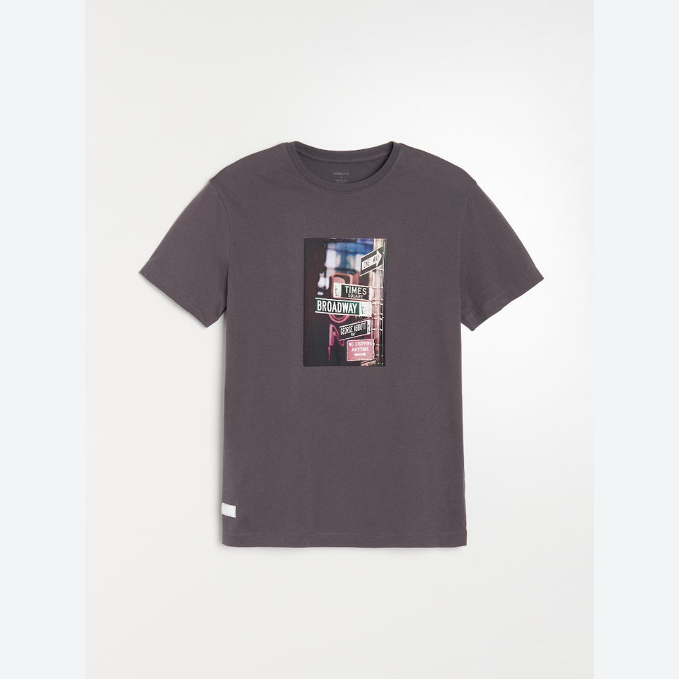 A dark gray crewneck t-shirt with a rectangular graphic print on the chest depicting a street scene with signs, photographed flat against a light gray background.