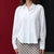 A woman wearing a white long-sleeve button-up shirt and a beige-and-black plaid skirt, standing against a split red and black background.