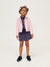 Young girl wearing a pink jacket, navy floral dress, and skirt on a white background
