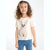 A young girl with curly brown hair wearing a cream-colored t-shirt with a large printed kitten graphic and blue jeans with small pink hearts, standing against a plain white background.
