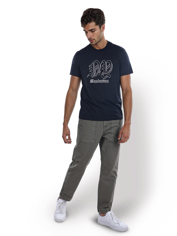 Man wearing a navy t-shirt with a logo and gray pants on a white background