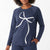 A woman wearing a heathered navy blue long-sleeve top with a large white bow graphic on the front, paired with matching navy pants, against a clean white background.