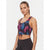 A woman modeling a sleeveless athletic crop top with a pink and blue tropical leaf print on a black background, paired with black leggings, against a light gray studio background.