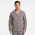 A man wearing a long-sleeve button-front pajama shirt with a subtle plaid pattern in gray, brown, and white, paired with matching plaid pajama pants, against a plain white studio background.