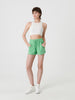 Woman wearing a white sleeveless top and green shorts on a white background