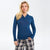 A blonde woman modeling a fitted long-sleeve polo shirt in a deep blue color, paired with gray and black plaid pants, against a plain white studio background.