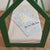 A light blue baby blanket featuring a polar bear illustration and the text 'Hi, I'm little bear' is draped over a mattress in a green house-shaped wooden bed frame.