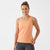 A woman wearing a peach-colored sleeveless athletic tank top and dark gray leggings, standing against a plain white studio background.