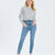 A woman modeling a light gray long-sleeve cropped cardigan and medium-wash blue skinny jeans against a plain white studio background.