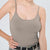 A woman wearing a fitted scoop-neck camisole tank top in taupe gray, paired with a patterned belt and pants, against a light gray studio background.