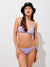 A woman modeling a lavender purple string bikini with a black bucket hat, standing against a plain white wall.