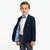 A young boy modeling a navy blue boys' blazer, styled with a white dress shirt, gray bow tie, gray trousers, and a light blue patterned lining visible on the open jacket pocket, against a plain white background.