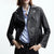 A woman wearing a black leather moto jacket over a light blue button-down shirt and dark jeans, photographed against a clean white studio background.
