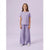 A young girl stands against a solid light purple studio background wearing a matching two-piece lounge set consisting of a short-sleeve crewneck t-shirt and wide-leg pants in a soft lavender color.