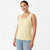 A woman modeling a pale yellow sleeveless knit tank top with scalloped edges and a textured pattern, paired with light blue jeans against a plain white studio background.