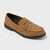A tan suede penny loafer shoe with a black sole, shown from a three-quarters angle on a light gray background.