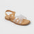 A single flat sandal with a tan footbed and sole, featuring clear transparent crisscross straps on a light gray background.