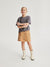 Young girl wearing a gray t-shirt and tan skirt with buttons on a white background