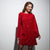 A woman wearing a long-sleeved red sequined mini dress, standing against a plain light gray studio background.