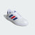 White Adidas sneaker with blue and red stripes on a light gray background