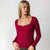 A woman modeling a long-sleeve scoop-neck top in deep burgundy, paired with leopard-print pants, against a plain light gray studio background.