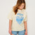 Young girl wearing a light-colored t-shirt with a graphic design on a plain background