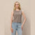 A blonde model wearing a sleeveless, textured taupe-brown button-front top and light-wash blue jeans, standing against a neutral beige textured wall.