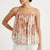 A woman wearing a sleeveless camisole top with thin straps and a pleated, gathered silhouette. The top features a dusty rose and cream floral pattern.