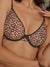 A close-up of a model wearing a leopard print bra with dark brown trim and thin shoulder straps.
