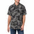 A man wearing a short-sleeve button-up shirt with a black background and a white tropical leaf print, paired with blue jeans, against a plain white background.