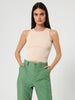 Woman wearing a beige sleeveless top and green pants on a white background