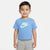 A young child wearing a light blue Nike short-sleeve t-shirt with a large white and light blue graphic on the chest, paired with light gray pants, set against a plain light gray background.