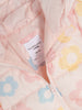 Close-up of a pink quilted jacket with floral patterns and a brand label.