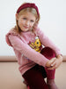 Young girl wearing a pink hoodie with a cartoon character, sitting on a beige surface.