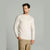 A man wearing a cream-colored long-sleeve mock neck sweater and khaki pants, standing against a solid light gray background.