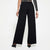 A model from the back wearing high-waisted, wide-leg black pants, a textured gray long-sleeve crop top, and black pointed-toe heels against a plain white studio background.
