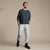 A man modeling a dark navy crewneck sweatshirt and light gray heather jogger pants against a solid beige studio background.