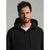 A man wearing a black hooded jacket over a white t-shirt, photographed against a neutral gray studio background.