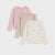 Three girls' long-sleeve tops arranged in a fan shape on a light gray background. The back top is light pink with a bow motif, the middle top is beige with white polka dots, and the front top is cream with a pink heart and bow pattern.