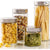 Four clear glass canisters with silver metal lids, filled with pasta, mixed grains, green lentils, and spaghetti, shown on a light reflective surface with a white background and a '4 pack' badge in the top right corner.