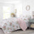Floral bedding set on a bed in a bright bedroom with white walls and wooden floor.