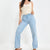 A model wearing light-wash blue wide-leg jeans and a cream-colored knit camisole top, standing against a plain white studio background.