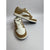 A pair of low-top sneakers in tan and white, with one shoe standing upright and the other resting on its side to show the side profile. The shoes feature a tan leather upper with white panels, white laces, and a white midsole.
