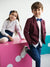 Two children in formal attire sitting on a pink surface with a white background