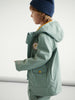 Person wearing a light green jacket with a logo on a white background