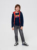 Child wearing a navy jacket with red hood, graphic t-shirt, gray pants, and black and white shoes on a white background