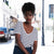 A woman standing on a sunlit street wearing a black and white horizontally striped short-sleeve top with a V-neck and a dark navy skirt.