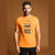 A man wearing a bright orange crewneck t-shirt with a black pumpkin graphic and the text 'BOOO TIME' printed on the front, posed against a solid brown studio background.