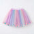 A pastel rainbow tulle tutu skirt with pom-pom trim, featuring vertical layers of pink, purple, blue, and yellow mesh with a matching elastic waistband.
